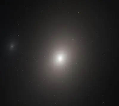 Hubble-Aufnahme der Galaxie M86 als diffuser, hell-weißer ovaler Lichtball, der zum Zentrum hin heller wird