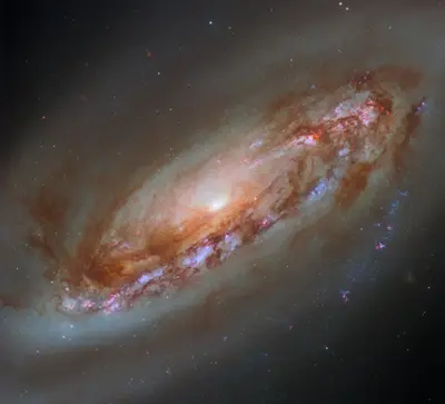 Hubble-Aufnahme der Spiralgalaxie M90 mit hellem Kern, rötlichen Staubwolken in der Scheibe und einem schwachen Gashalo